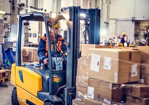 Man med hjälm kör truck och lastar lådor, tänker på finansiering för grossister